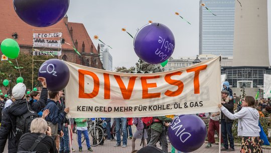 Banner auf Demonstration, auf dem steht "Divest. Keine Investitionen in Öl, Gas und Kohle"